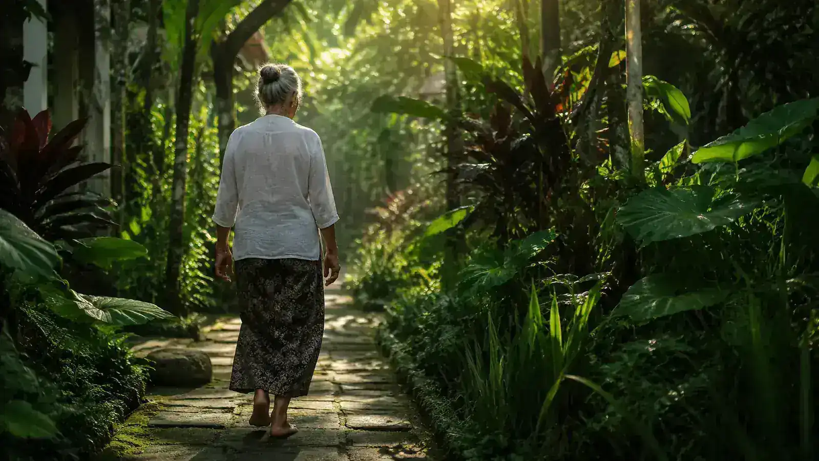 Person walking barefoot on a short garden path among tropical plants in morning light, moving with ease