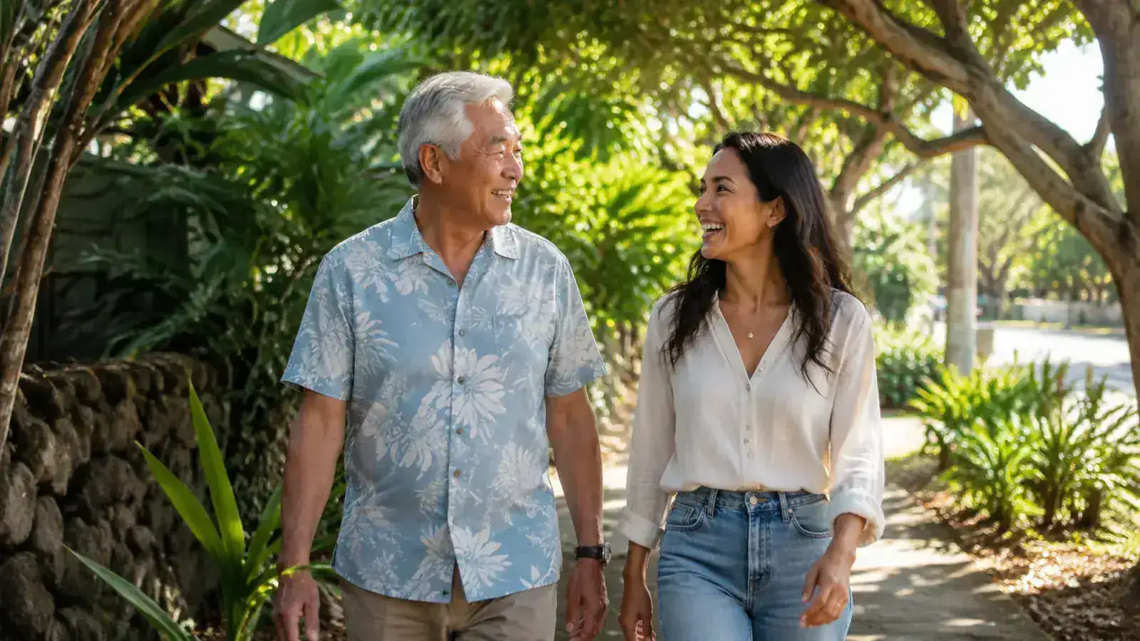 Older man and a younger family member walking on a shaded neighborhood path through tropical trees, mid-conversation, relaxed